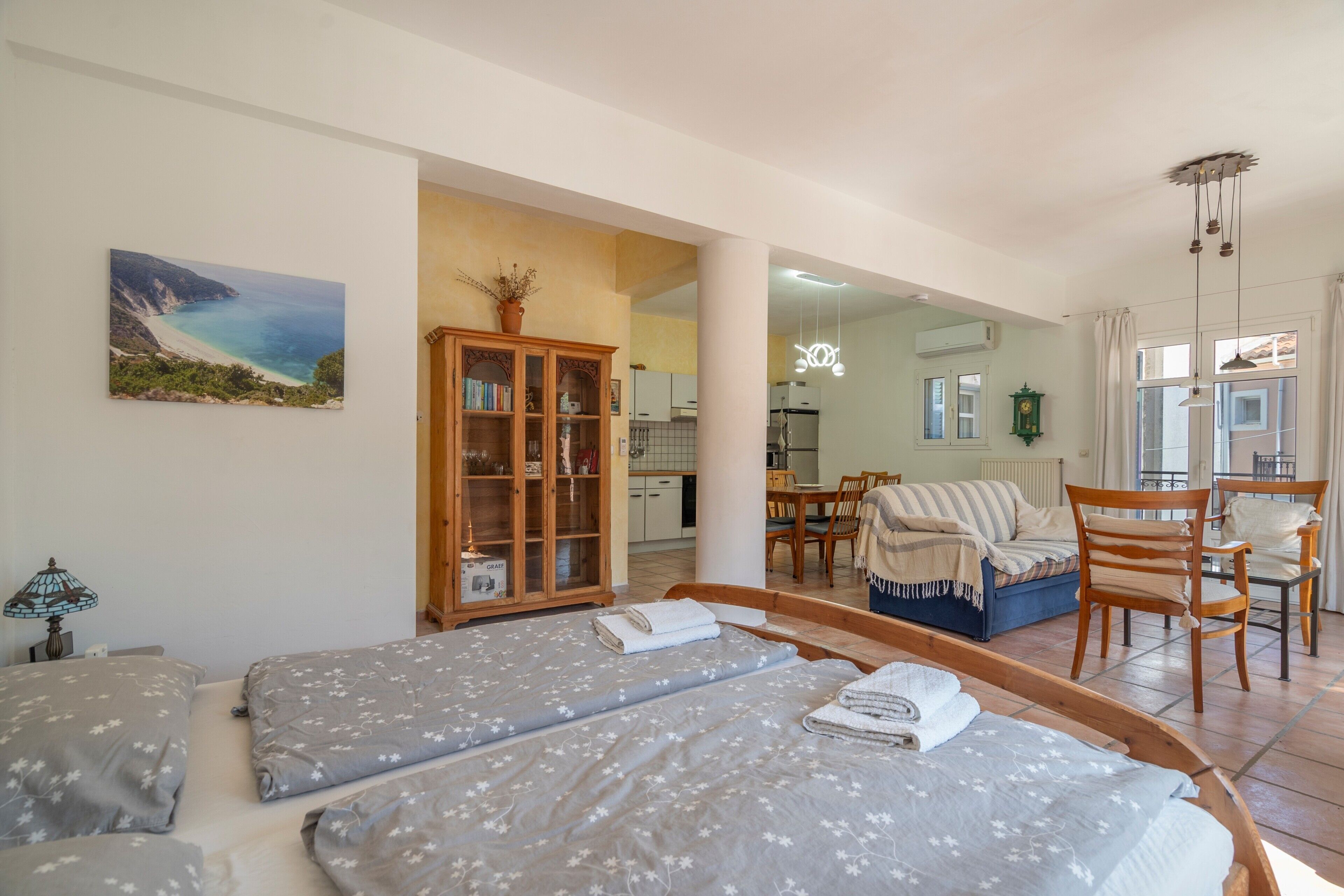 A bedroom with two beds, a wooden cabinet, a dining area, and a view of the kitchen.