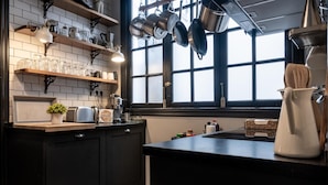 Une cuisine avec des meubles de couleur noire, un plan de travail noir, des casseroles suspendues et une fenêtre donnant sur un beau paysage.