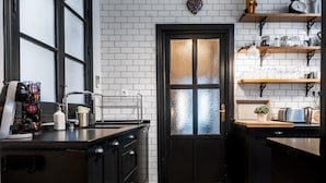 Une cuisine avec une porte noire, des murs recouverts de carreaux blancs et un sol à carreaux.