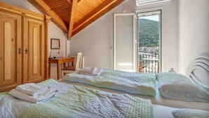 Un dormitorio con dos camas, vigas de madera en el techo, vista a un balcón y un armario de madera.