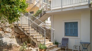 Una escalera de piedra que lleva a un balcón, una planta en maceta, dos sillas y una mesita.