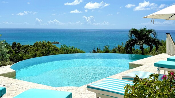 Une piscine d’un bleu éclatant, avec vue sur l’océan, entourée de verdure et de chaises longues.