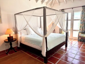A four-poster bed with a white canopy, a bedside table with a lamp, and a view of the outside through a door. - Private 4BR Oceanview Villa - Private Pool - Peaceful Hilltop Setting (Crab Hill)