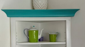 Une étagère à la couleur turquoise, ornée d’un ananas, avec deux théières vertes, un pichet violet et un panneau turquoise sur lequel on peut lire « PLAGE ».