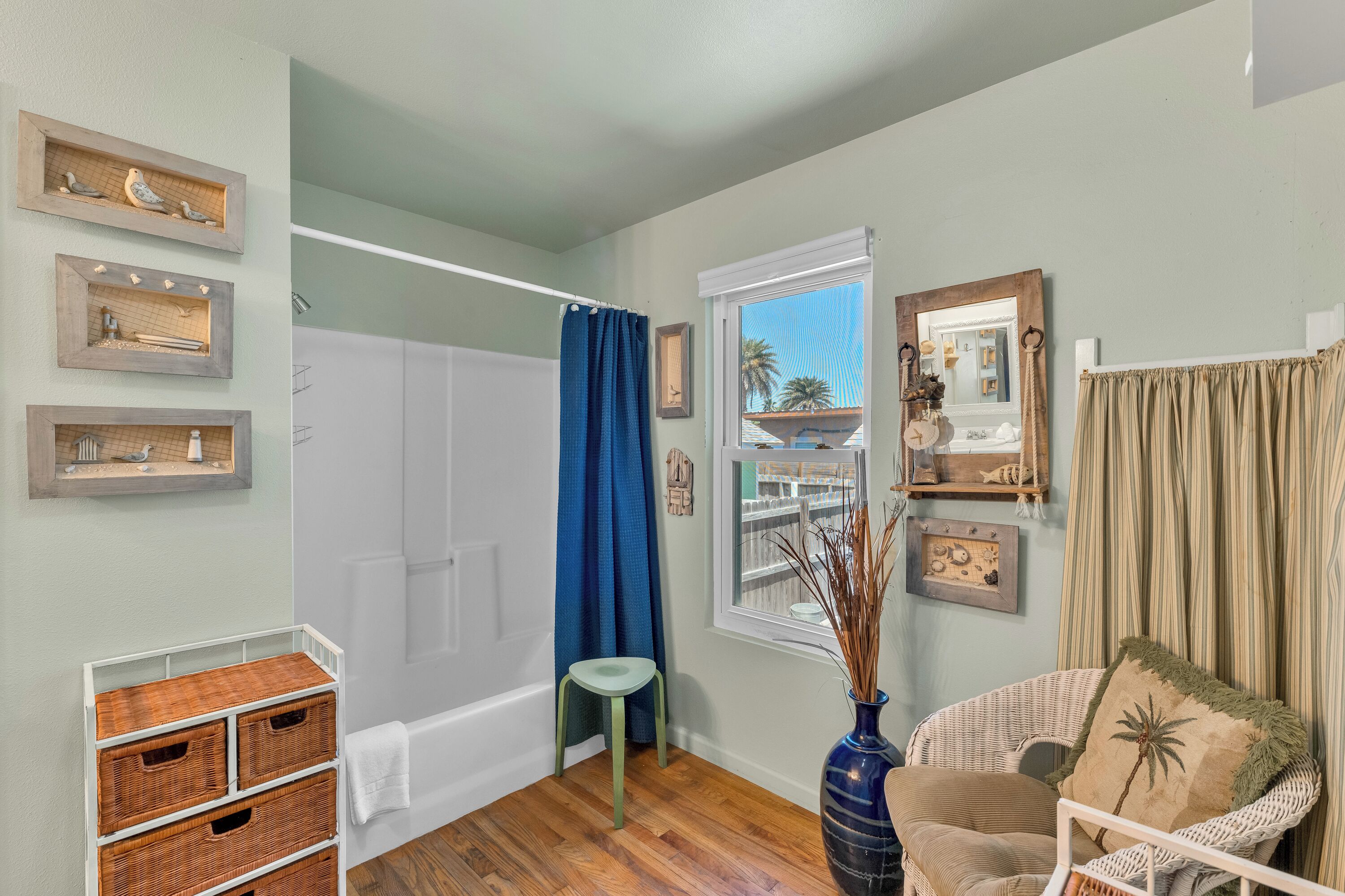 A bathroom with a bathtub, a shower, a window with a view, a chair, and wicker baskets.
