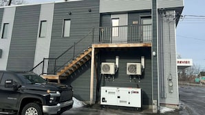 Un edificio de dos plantas con fachada gris, una escalera de madera y un letrero que dice "REVIER".