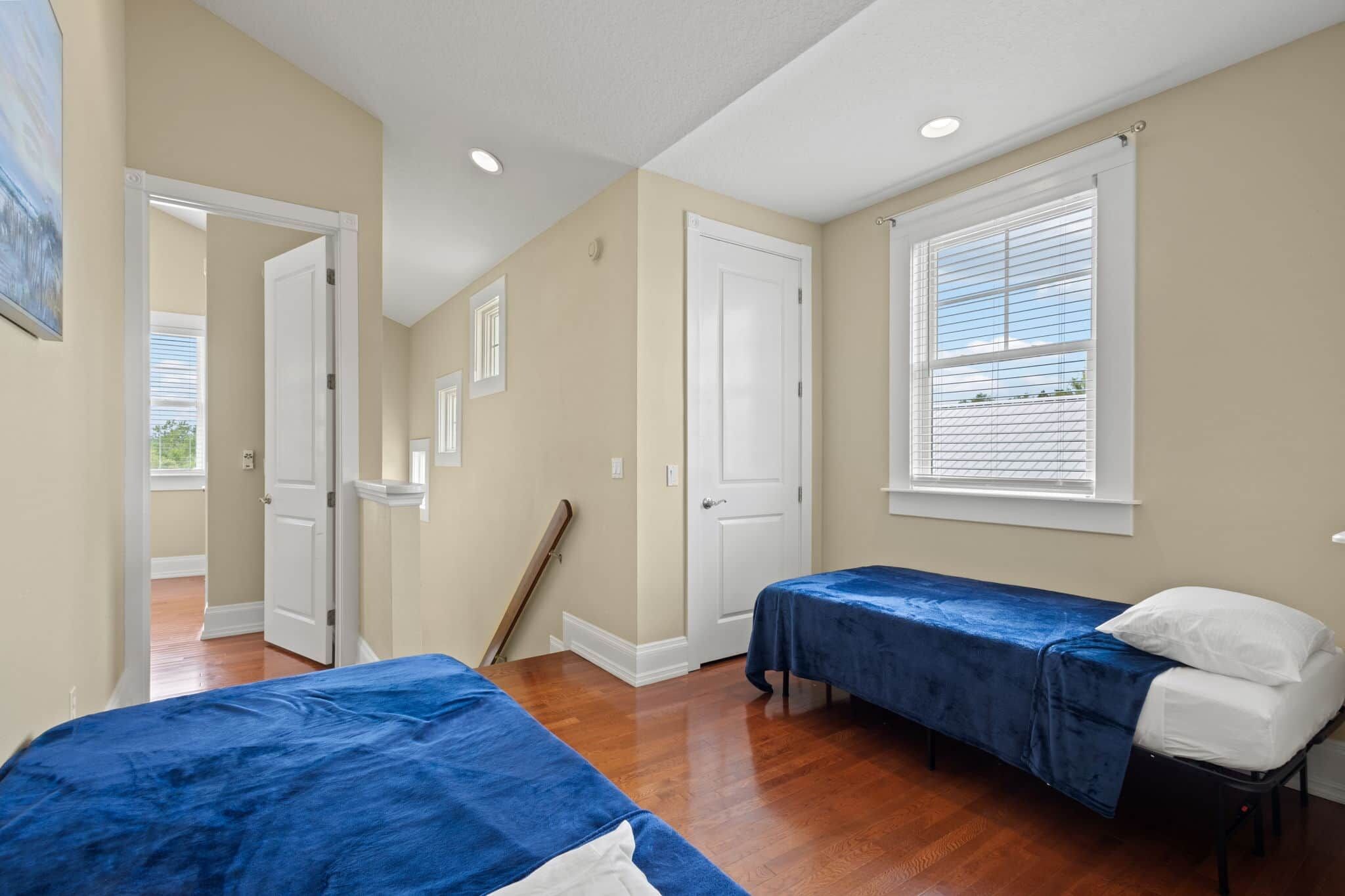 A bedroom with two beds, a window with blinds, a door, and a wooden floor.