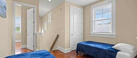 A bedroom with two beds, a window with blinds, a door, and a wooden floor.