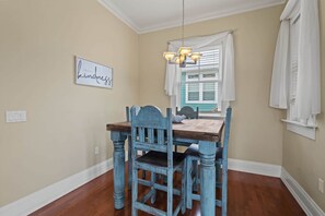 A dining area with a wooden table and chairs, a chandelier, and a window with white curtains. - Driftwood Haven at Rivers Bend - Steinhatchee (Steinhatchee)