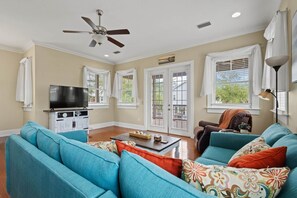 A living room with teal sofas, a coffee table, a TV, and a ceiling fan. - Driftwood Haven at Rivers Bend - Steinhatchee (Steinhatchee)
