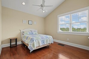 Ein Schlafzimmer mit Bett, Deckenventilator, Fenster mit Jalousien und einem kleinen Tisch.