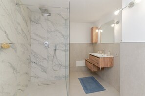 Un baño moderno con ducha de vidrio, tocador de madera y espejo con iluminación.