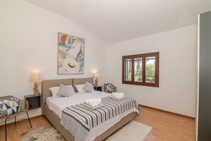 Een slaapkamer met een groot bed, een schilderij aan de muur, een raam en een stoel.