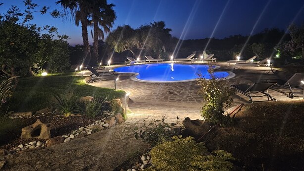 Un área de piscina iluminada durante la noche, con sillones reclinables.