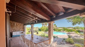 Un patio al aire libre con una mesa y sillas de madera, un muro de piedra y vista a una piscina.