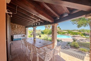 Un patio al aire libre con una mesa y sillas de madera, un muro de piedra y vista a una piscina.