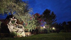 Un jardín con una formación rocosa, plantas en flor y una zona bien iluminada.