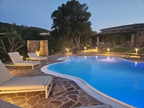 Una piscina con sillones de descanso, suelo de piedra y una pared de piedra.