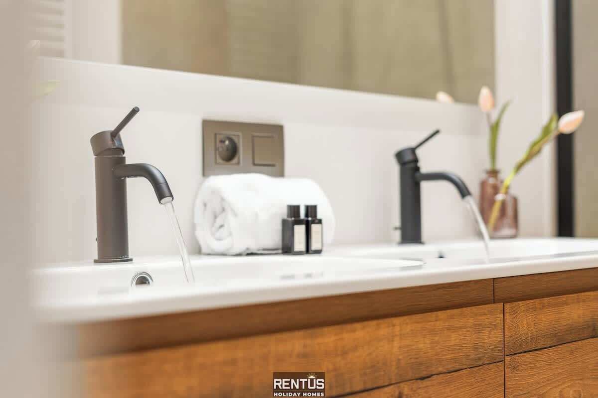 A bathroom with a white sink, two black faucets, a towel, and a small vase with flowers.