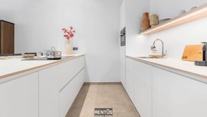 A modern kitchen with white cabinetry, a wooden countertop, a built-in oven, and a shelf with decorative items. - Beach Loft - luxury apartment with sea view in Ostend (Oostende)