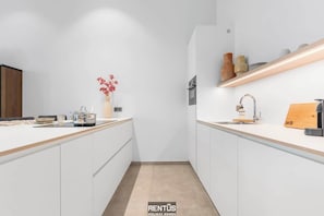 Eine moderne Küche mit weißen Schränken, einer Holz Arbeitsplatte, einem eingebauten Backofen und einem Regal mit Dekoration.
