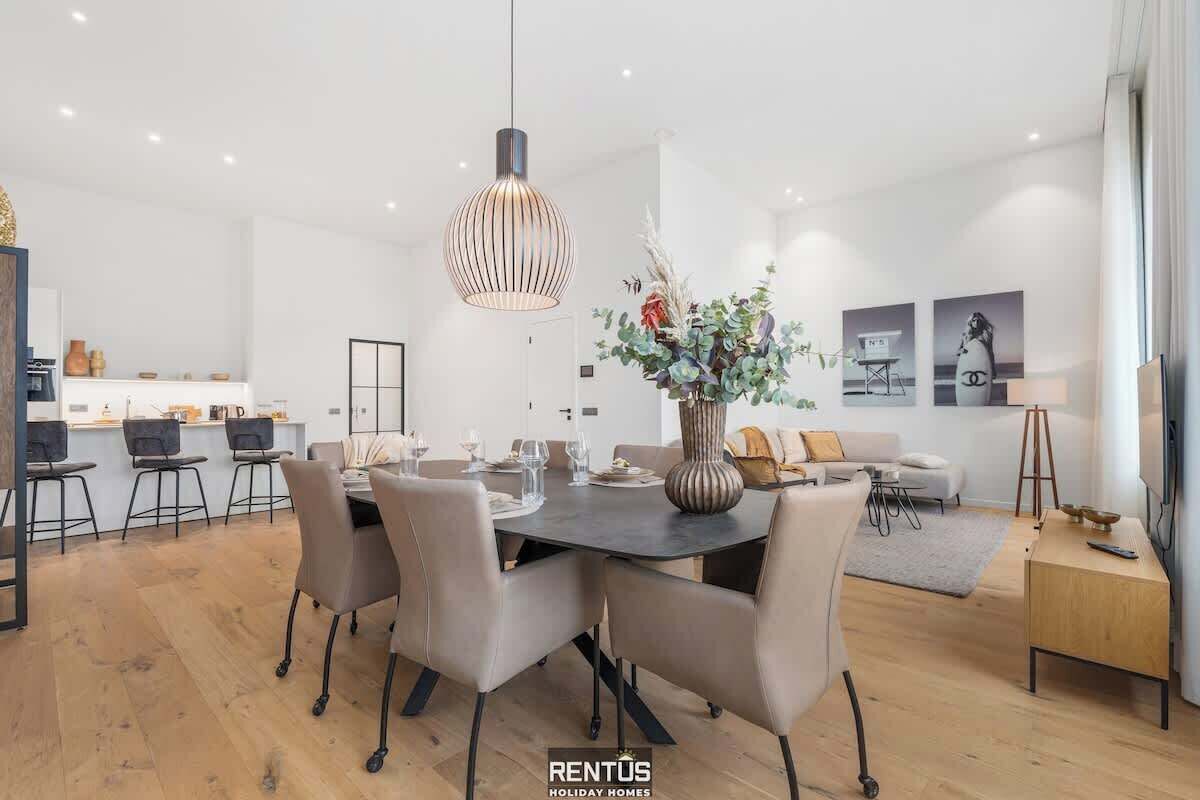 Una sala moderna con comedor, un jarrón grande con flores y un sofá.