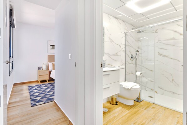 A modern bathroom with a marble backsplash, a glass shower enclosure, and a wooden floor. - Apartamento Velapi 23 (Los Alcazares) (San Javier)