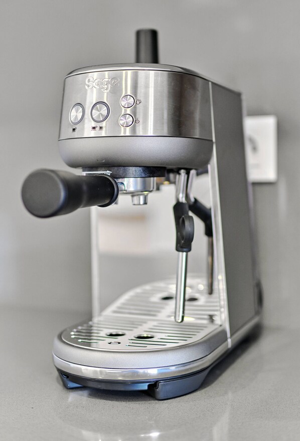 A compact, stainless steel espresso machine with a digital display and a single control knob.