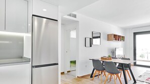 Une cuisine moderne dotée d’un réfrigérateur en acier inoxydable, d’un coin repas avec une table et des chaises, et d’une grande fenêtre qui laisse entrer la lumière naturelle.