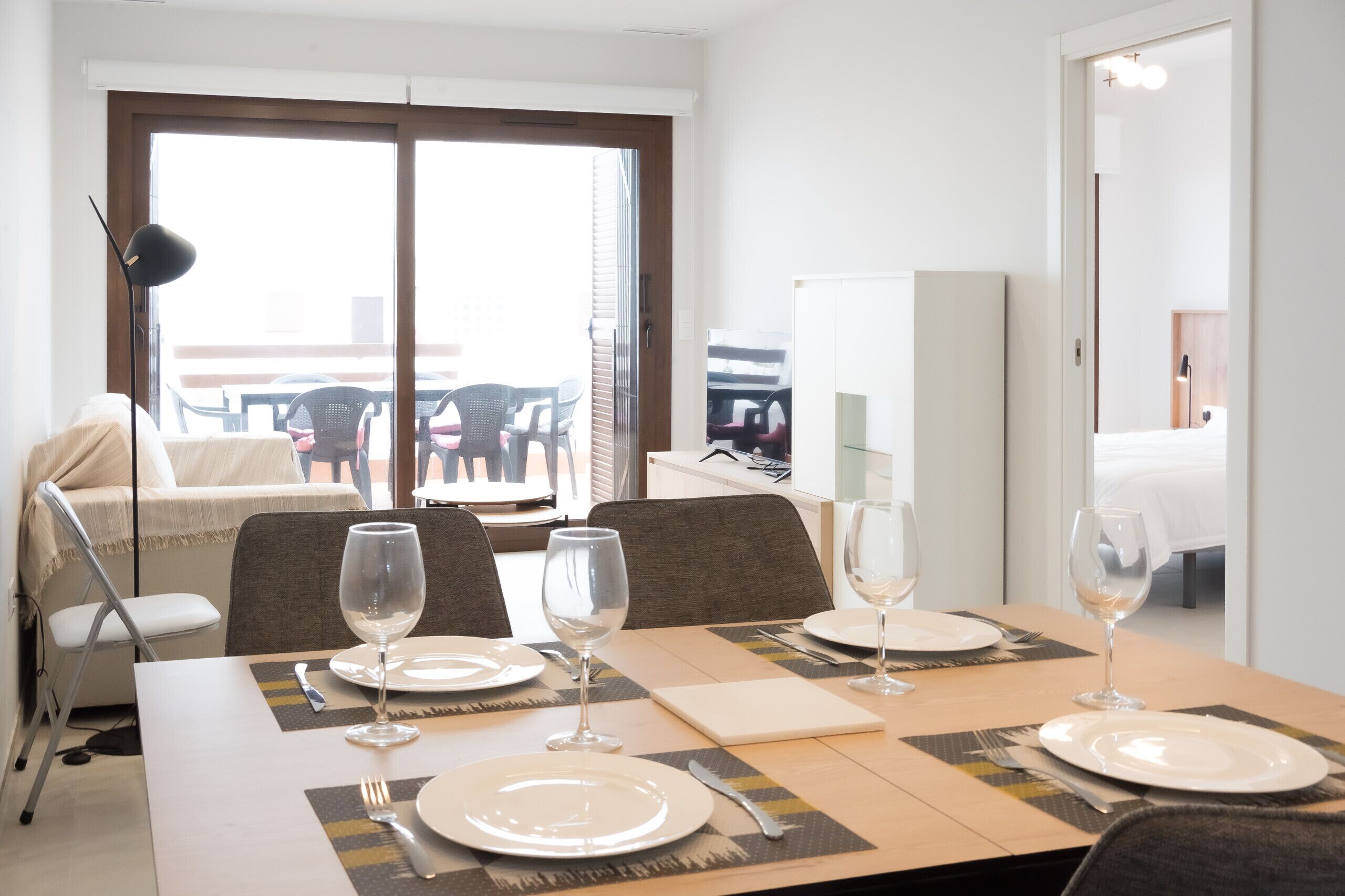 A dining area with a table set for four, including wine glasses and plates, in a room with a large window and a view of the outside.