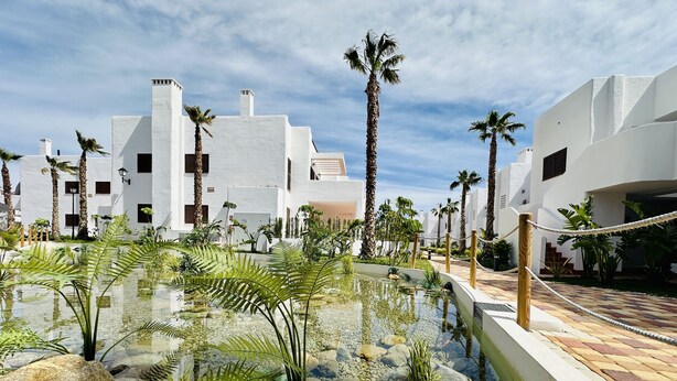 Un resort con area piscina circondata da palme e rocce, edifici bianchi e una barriera di corde.