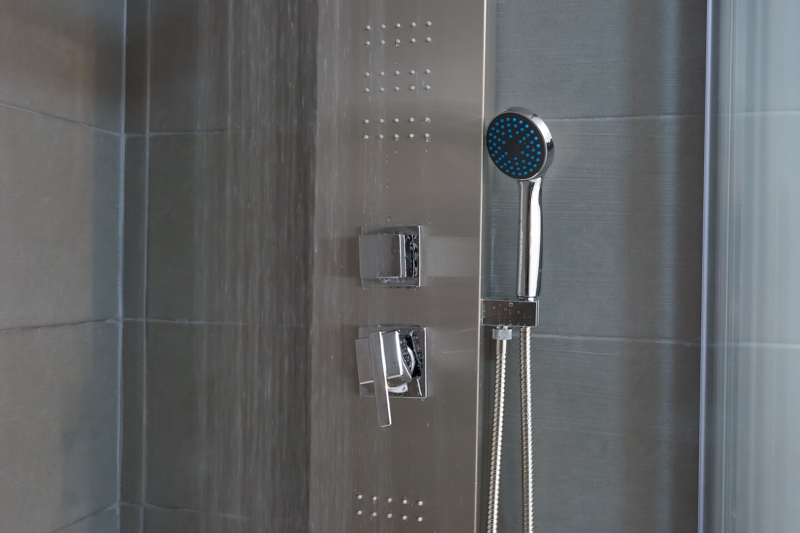 A modern shower with a handheld showerhead and a fixed wall-mounted control panel.