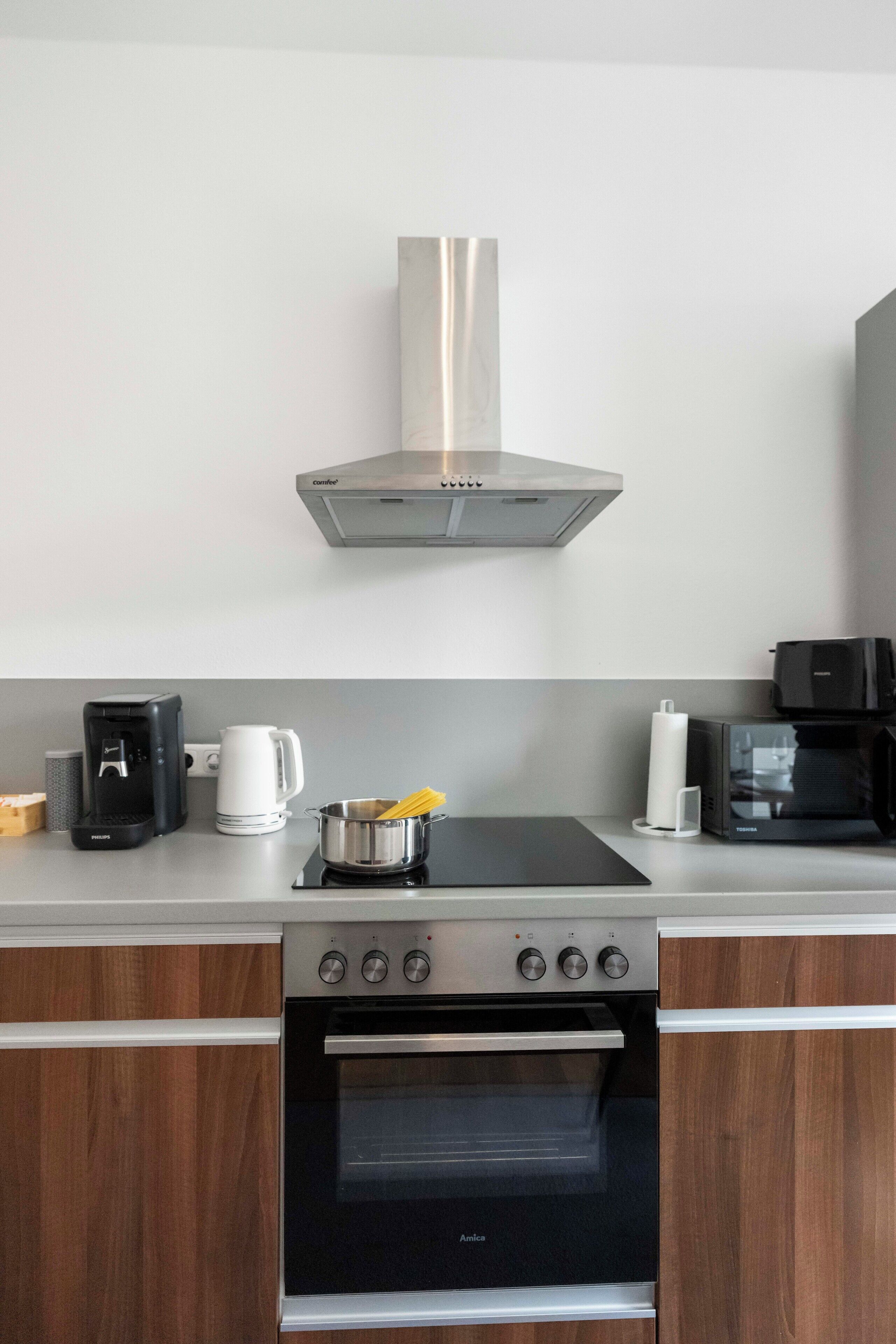 A modern kitchen with a built-in oven, a coffee maker, a kettle, and a microwave.