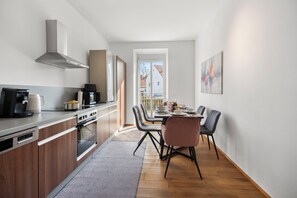 Eine moderne Küche mit Essbereich, ausgestattet mit Backofen, Kaffeemaschine und Esstisch mit Stühlen.