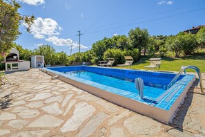 Ein Swimmingpool mit einer Steinterrasse, Liegestühlen und einem Grillbereich.