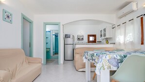 Un espace de vie compact comprenant un coin cuisine, un coin repas et une salle de bain visible à travers une porte ouverte.