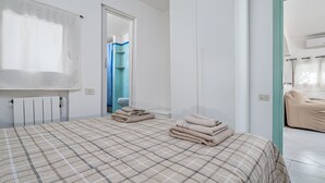 Une chambre à coucher avec un lit, un radiateur, une salle de bain visible à travers une porte ouverte et un rideau de douche.