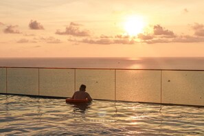 Eine Person sitzt in einem Pool mit Blick auf den Sonnenuntergang.