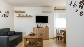 Una sala de estar moderna con un sofá, una mesa de centro de madera, un televisor y un comedor con mesa y sillas.