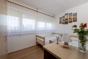 Ein Schlafzimmer mit einem hölzernen Bett, einem Nachttisch mit Lampe, einem Fenster mit durchscheinenden Vorhängen und einer Wand mit gerahmten Bildern.