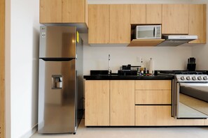Una cocina moderna con armarios de madera, un refrigerador de acero inoxidable, un microondas, una estufa y un fregadero.