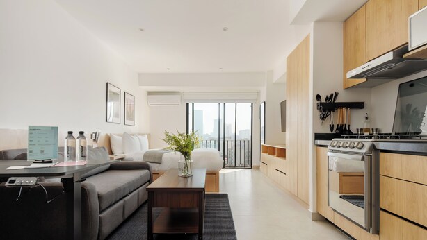 A modern living room with a sofa, coffee table, and a view of the city through large windows. - Via Insurgentes by Wynwood House (Mexico City)