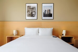 Habitación de hotel con una cama grande, dos mesitas de noche con lámparas, y dos cuadros en la pared.