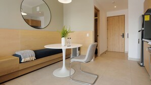 A modern living area with a round white table, a grey chair, a black sofa with a patterned throw, a round mirror on the wall, and a wooden door in the background. - Via Insurgentes by Wynwood House (Mexico City)