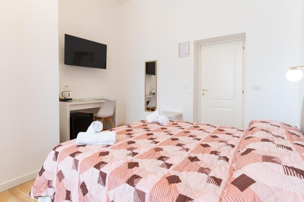 Un dormitorio con cama, escritorio, silla, televisor montado en la pared y una puerta.