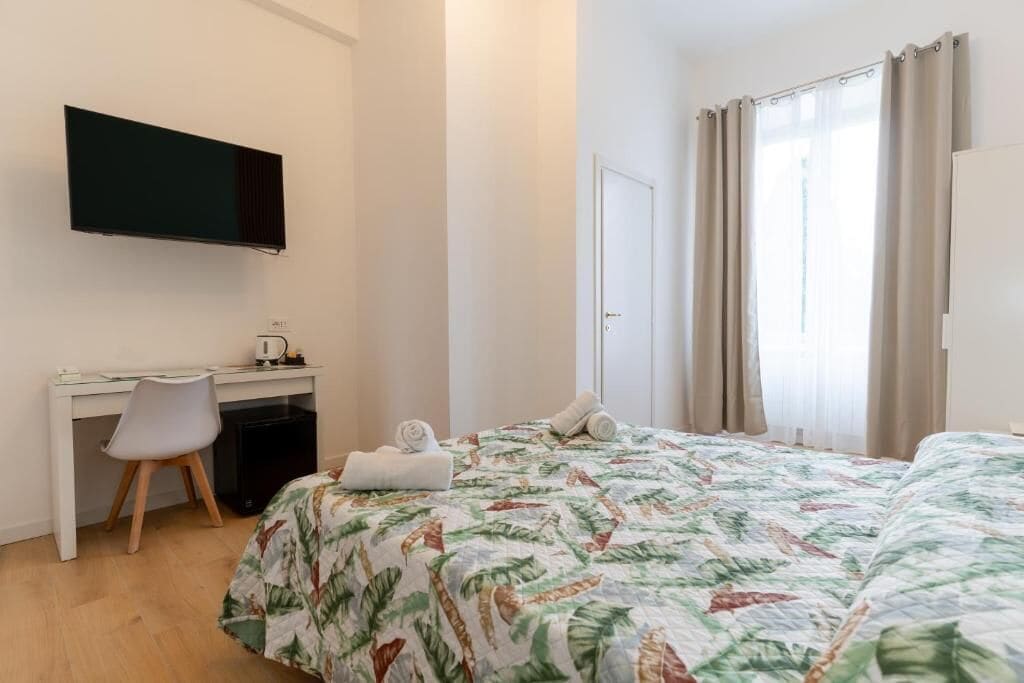 Ein Hotelzimmer mit Bett, Schreibtisch, Stuhl, Fernseher und einem fenster mit Vorhängen.
