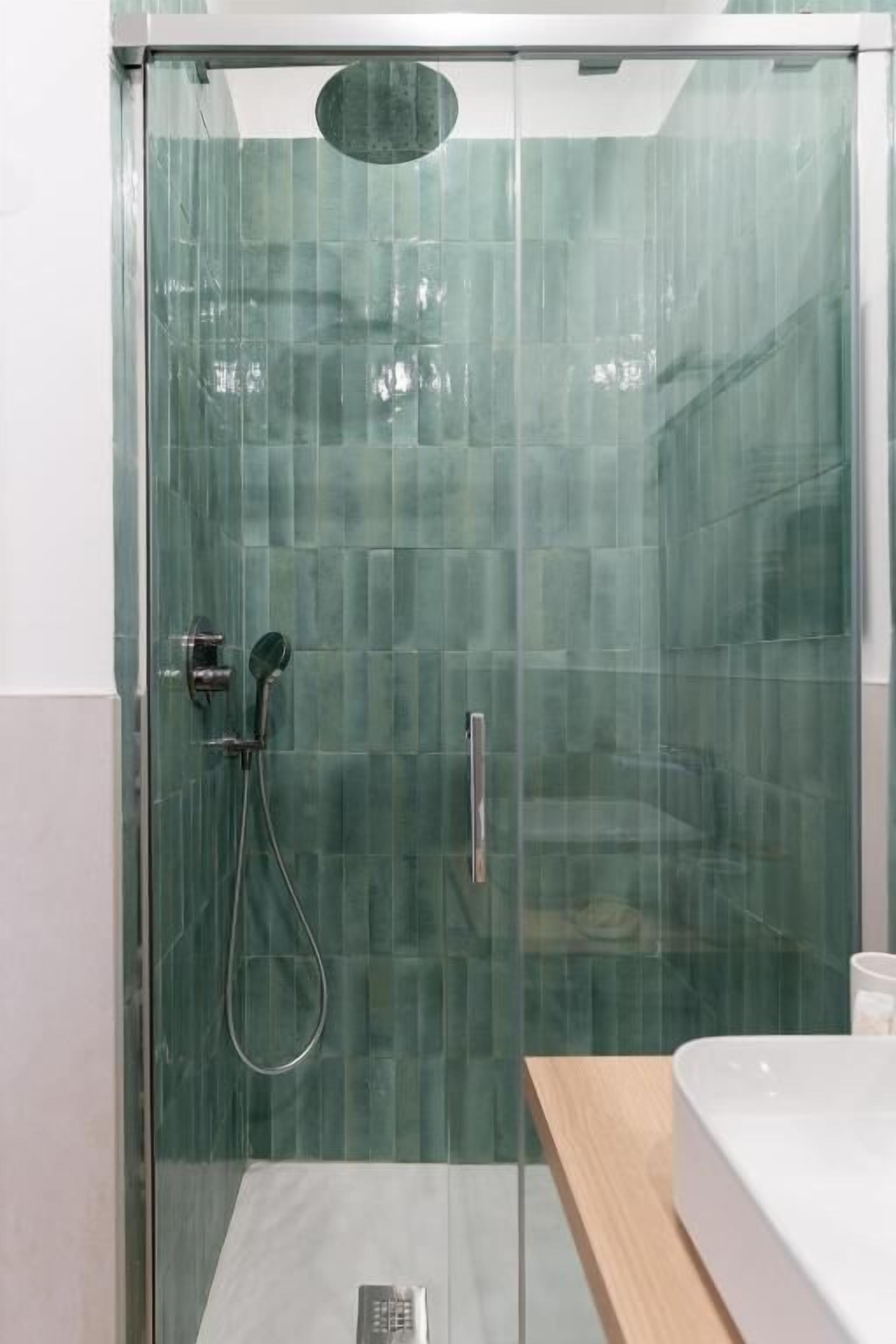 A glass-enclosed shower with a handheld showerhead and a wall-mounted faucet.