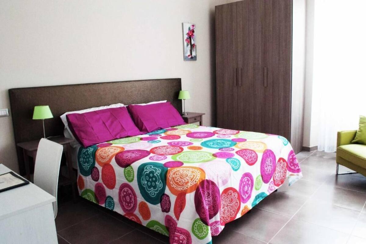 Un lit recouvert d’une couvre-lit aux motifs colorés, deux lampes de chevet, une table de chevet et un fauteuil vert.
