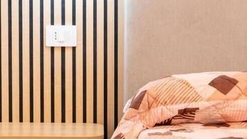 A bedroom with a bed, a bedside table, a wall-mounted light, and a wooden panel wall.