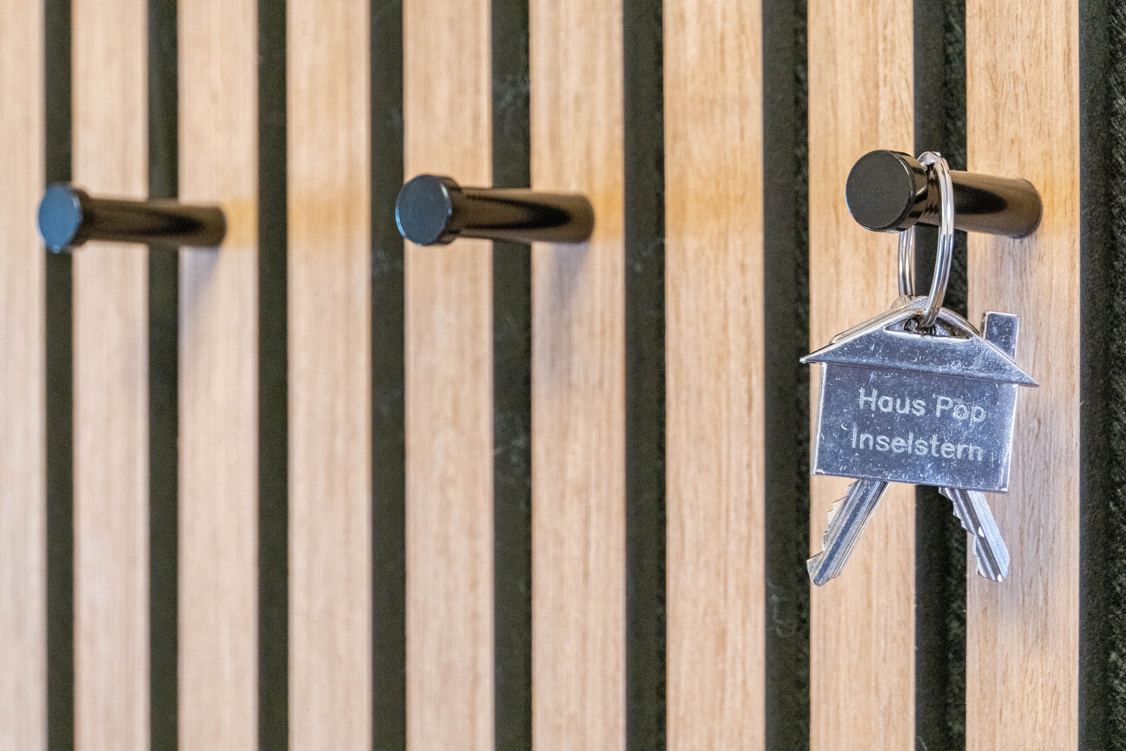 A set of keys with a label 'Haus Pop Inselstern' hanging on a wooden wall with vertical slats.